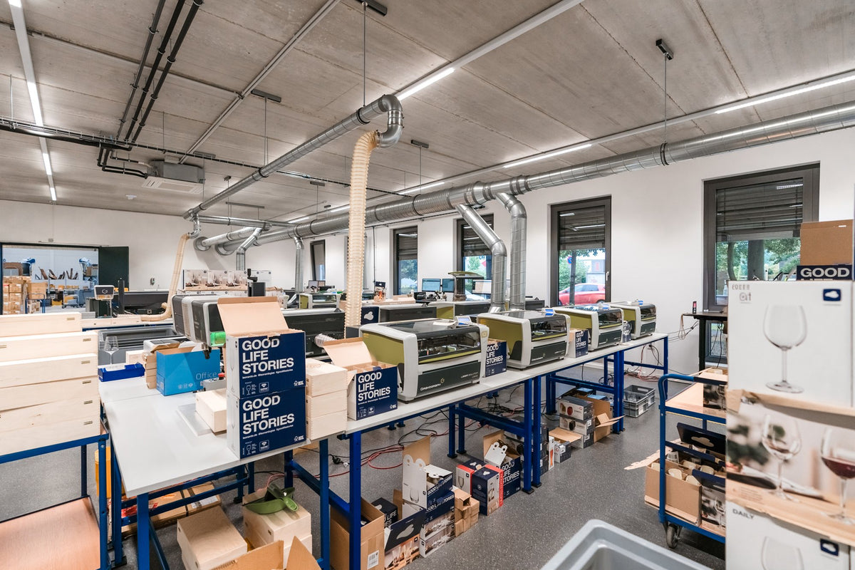 Lasergravur-Arbeitsplaetze auf blauen Werkbaenken mit Absaugung an der Hallendecke